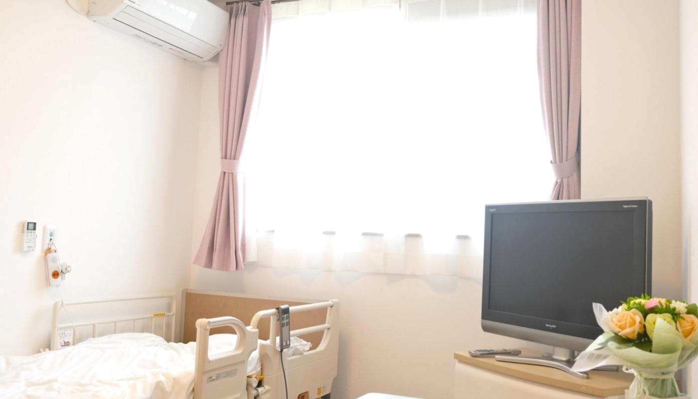 介護ベッド、テレビ、花が置かれた明るい個室。エアコン完備。
