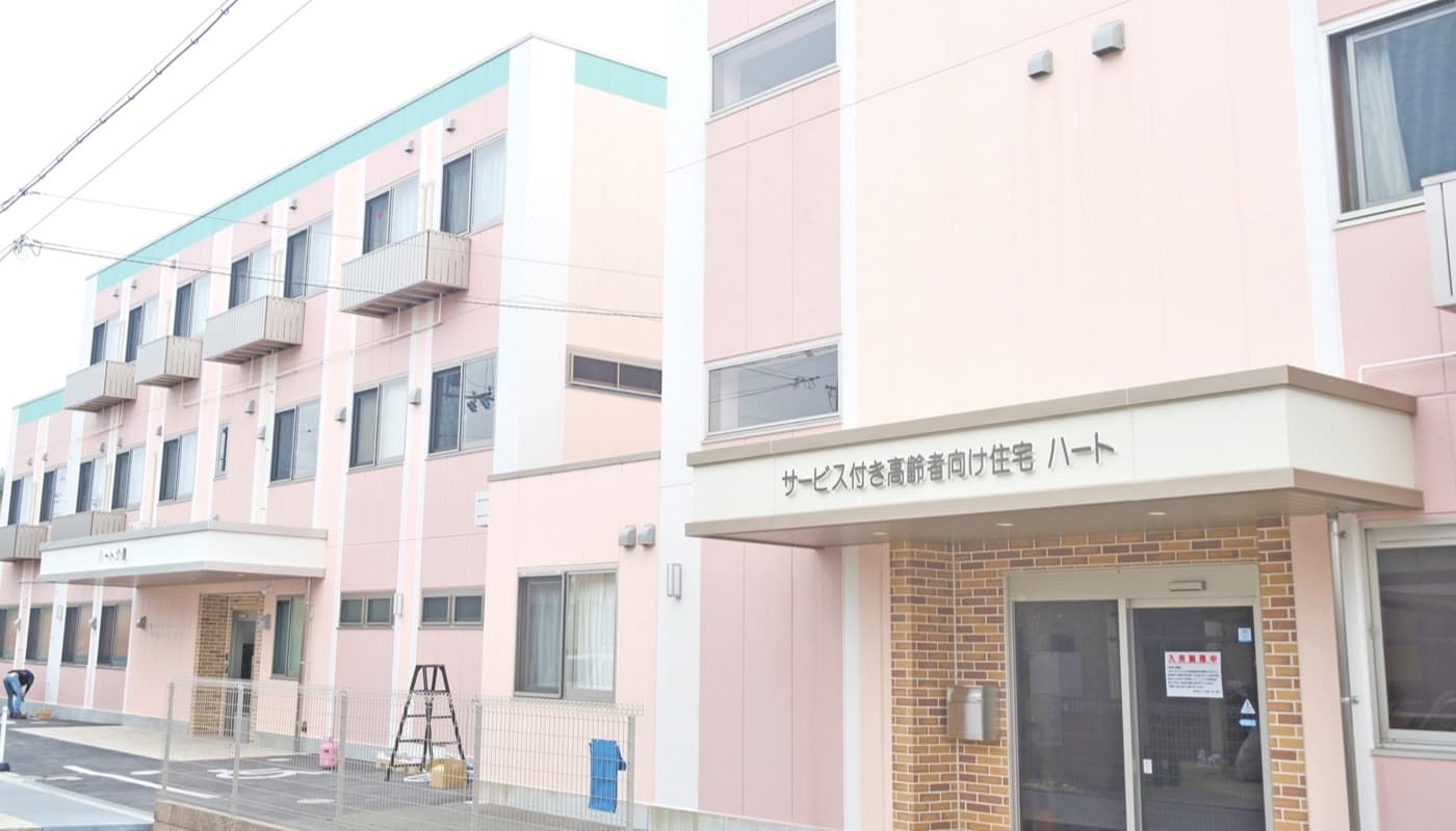 ピンク色の外壁が特徴の介護施設建物の外観。玄関入口が見える。
